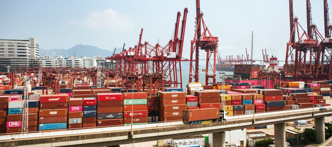 services-03 A bustling scene of cargo containers and cranes at a Hong Kong port, showcasing global trade.