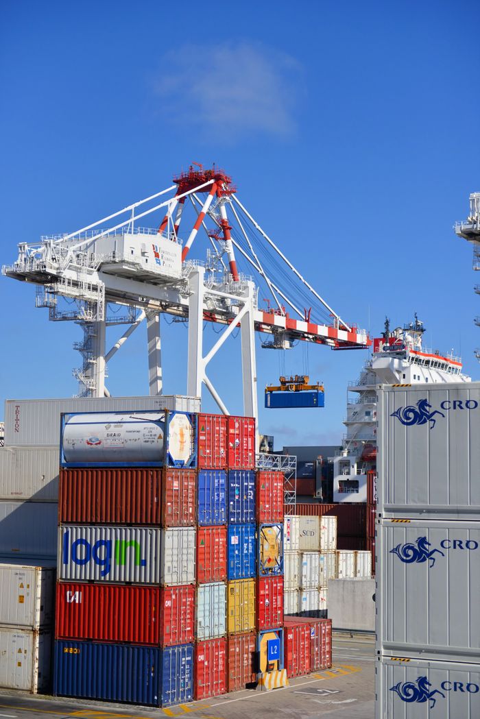 about-01 Colorful shipping containers stacked in a busy port with cranes overhead.