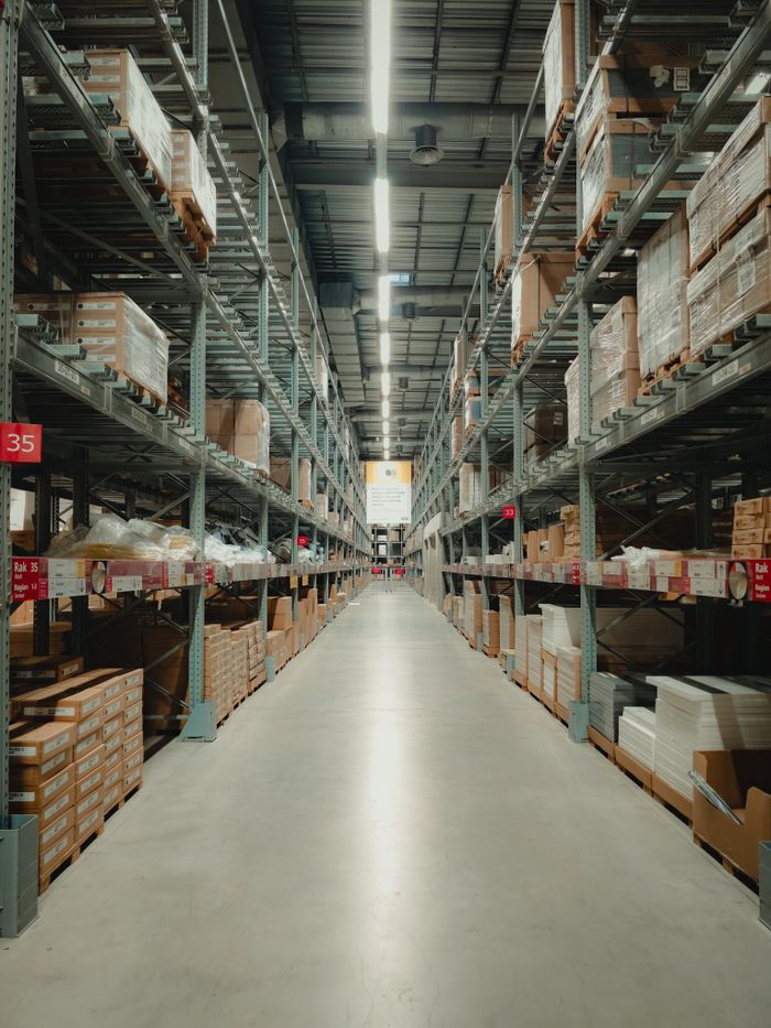 ours-journey Spacious warehouse aisle with shelves filled with neatly stacked products and pallets.
