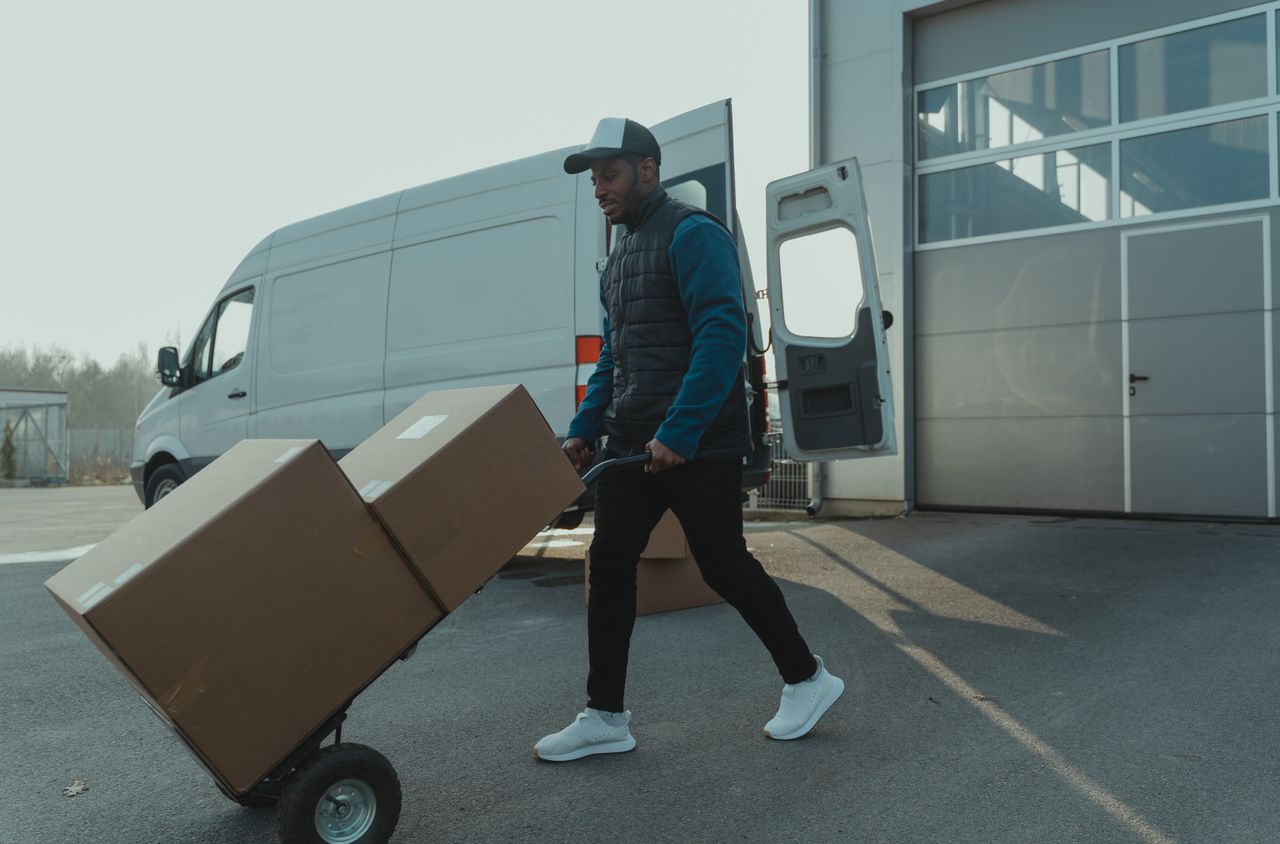 services-02 Courier pushing a trolley with boxes near a van at a warehouse, showcasing delivery services.